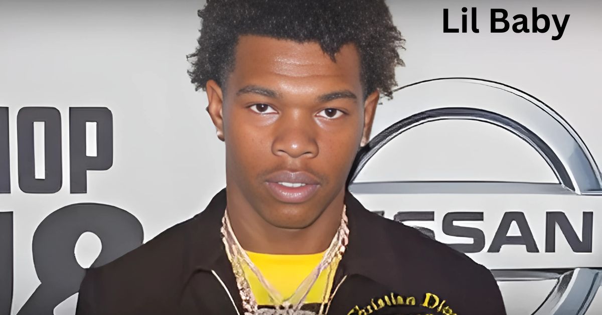 The rapper is wearing a black jacket and standing in front of a car