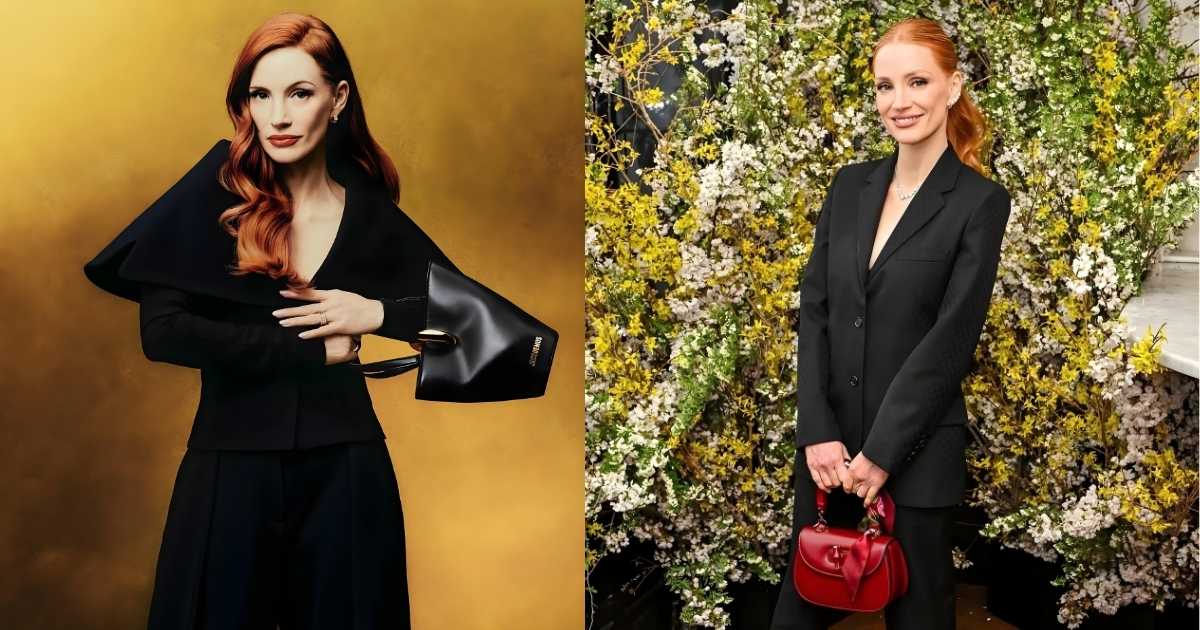 a person in a black suit and red purse standing in front of a wall of flowers